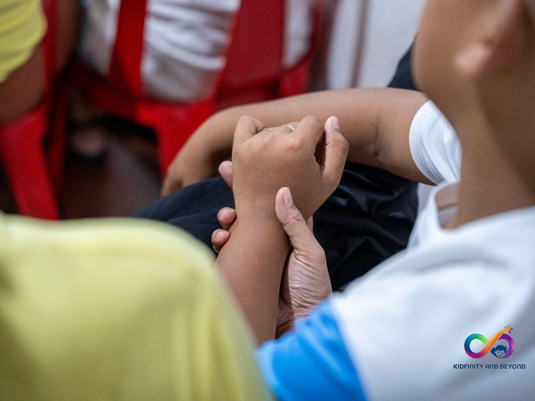 Close-up of an adult’s hand holding a child’s wrist, the child wearing a white shirt with a blue sleeve.